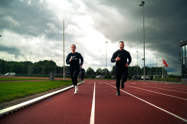 Twee mensen rennen op een atletiekbaan in de buitenlucht.